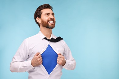 Photo of Happy businessman wearing superhero costume under suit on light blue background. Space for text