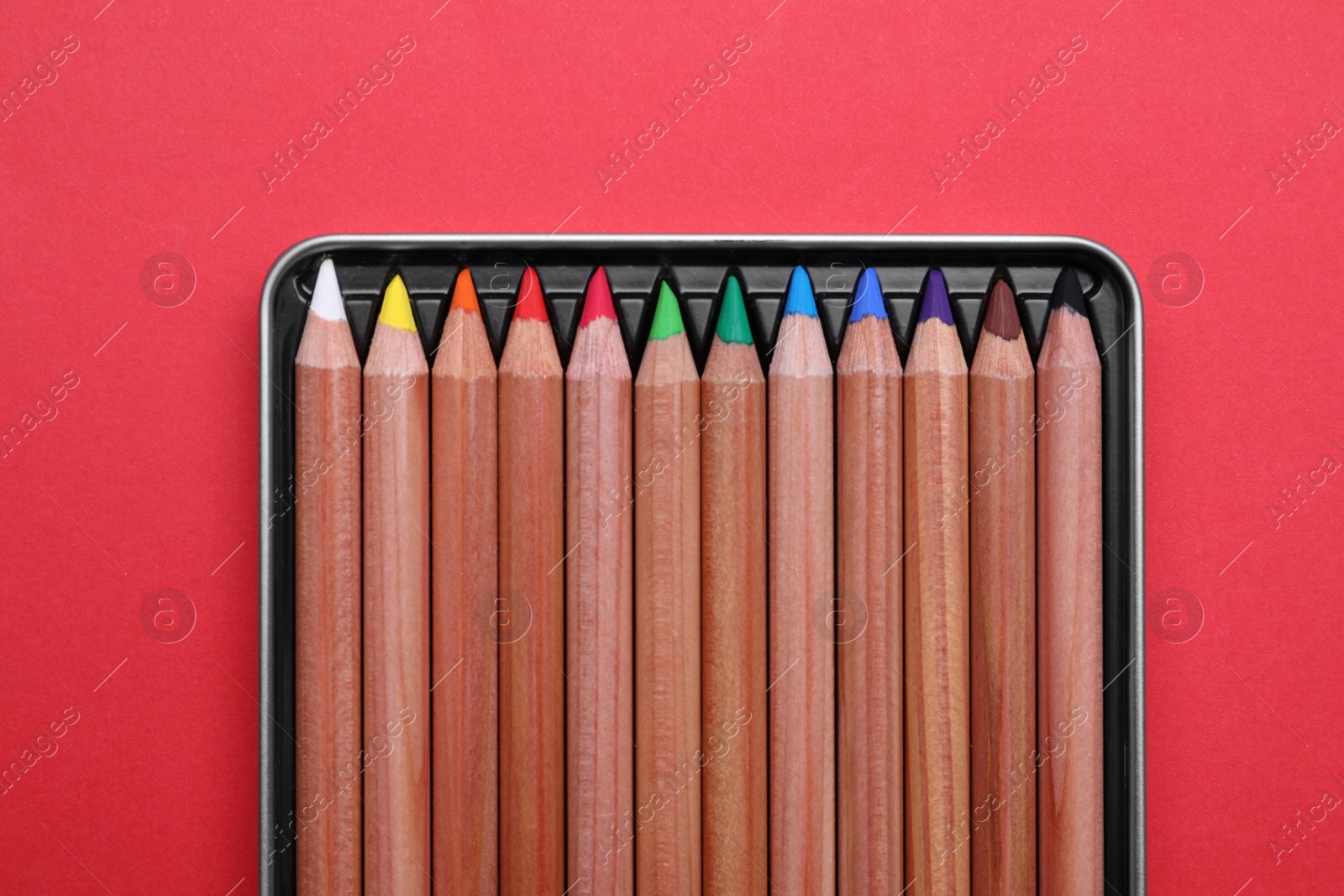 Photo of Box with many colorful pastel pencils on red background, top view. Drawing supplies