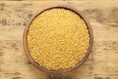 Bowl of uncooked bulgur on wooden table, top view