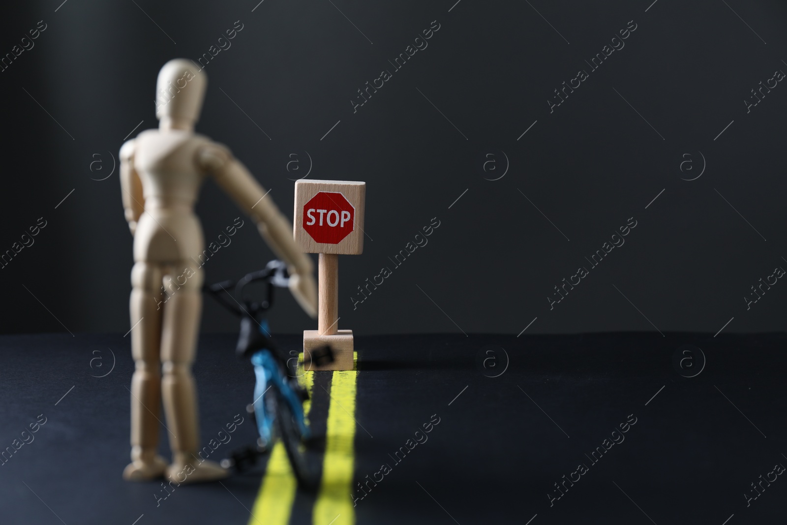 Photo of Development through barriers overcoming. Road Stop sign blocking way for wooden human figure with toy bicycle, space for text