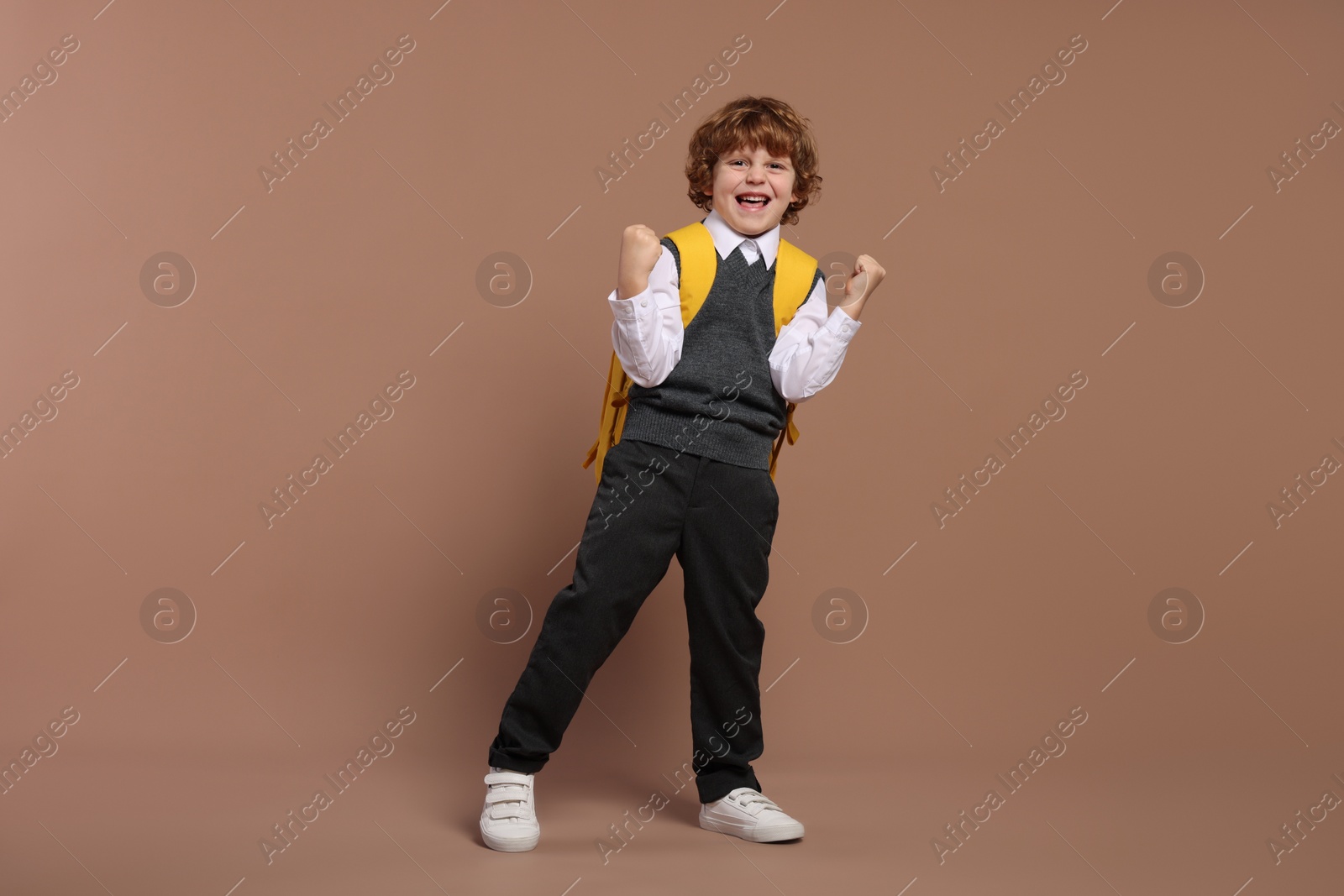 Photo of Emotional schoolboy with backpack on brown background