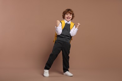 Emotional schoolboy with backpack on brown background