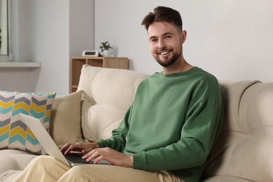 Photo of Handsome man with laptop sitting on sofa at home