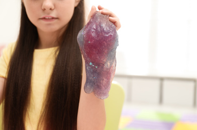 Photo of Little girl playing with slime in room, closeup