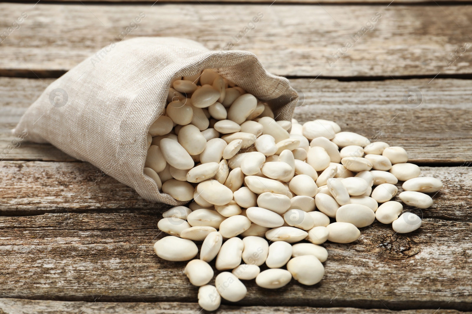 Photo of Overturned sack with white beans on wooden table