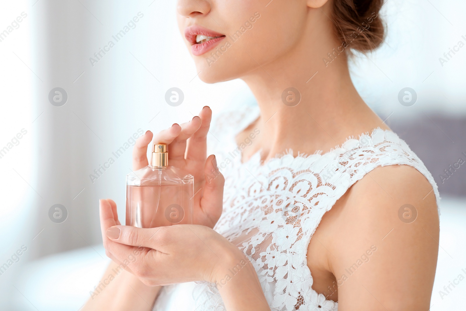Photo of Beautiful young bride with bottle of perfume on blurred background, closeup