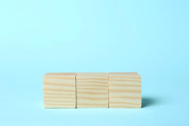 Photo of Wooden cubes on light blue background, space for text. Idea concept