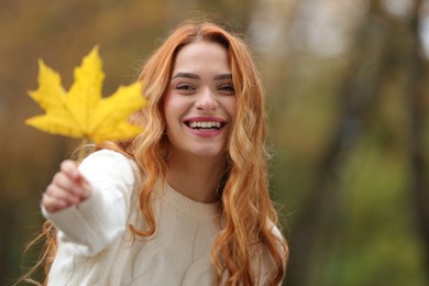 Photo of Portrait of smiling woman showing autumn leaf outdoors, selective focus. Space for text