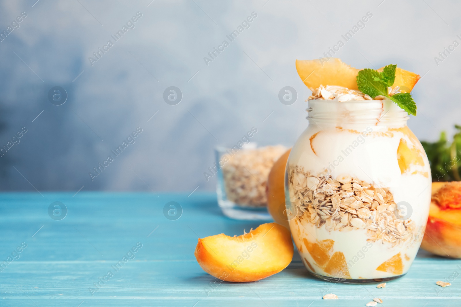 Photo of Tasty peach dessert with yogurt and granola on light blue wooden table. Space for text