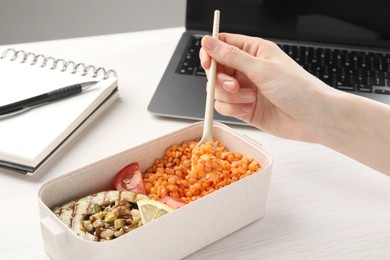 Photo of Woman eating healthy products high in vegetable fats near laptop at wooden table, closeup