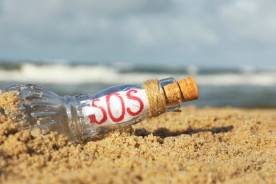 Photo of Glass bottle with SOS message on sand near sea, closeup