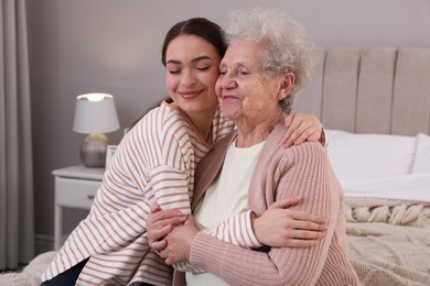 Photo of Young caregiver talking to senior woman in bedroom. Home health care service