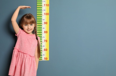Little girl measuring her height on color background