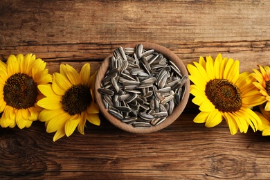 Photo of Raw sunflower seeds and flowers on wooden table, flat lay