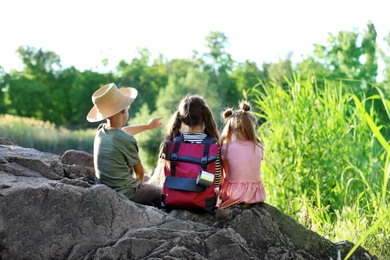 Photo of Little children sitting on rock outdoors. Summer camp