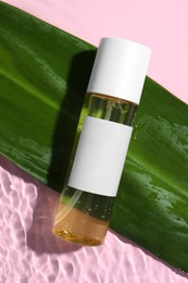 Bottle of cosmetic oil with green leaf in water on pink background, flat lay