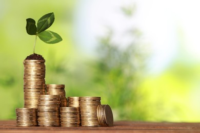 Photo of Stacked coins and green sprout on wooden table against blurred background, space for text. Investment concept