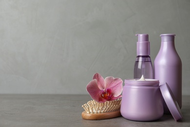 Photo of Different hair products, flower and brush on grey table. Space for text