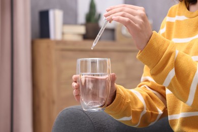 Woman dripping food supplement into glass of water indoors, closeup