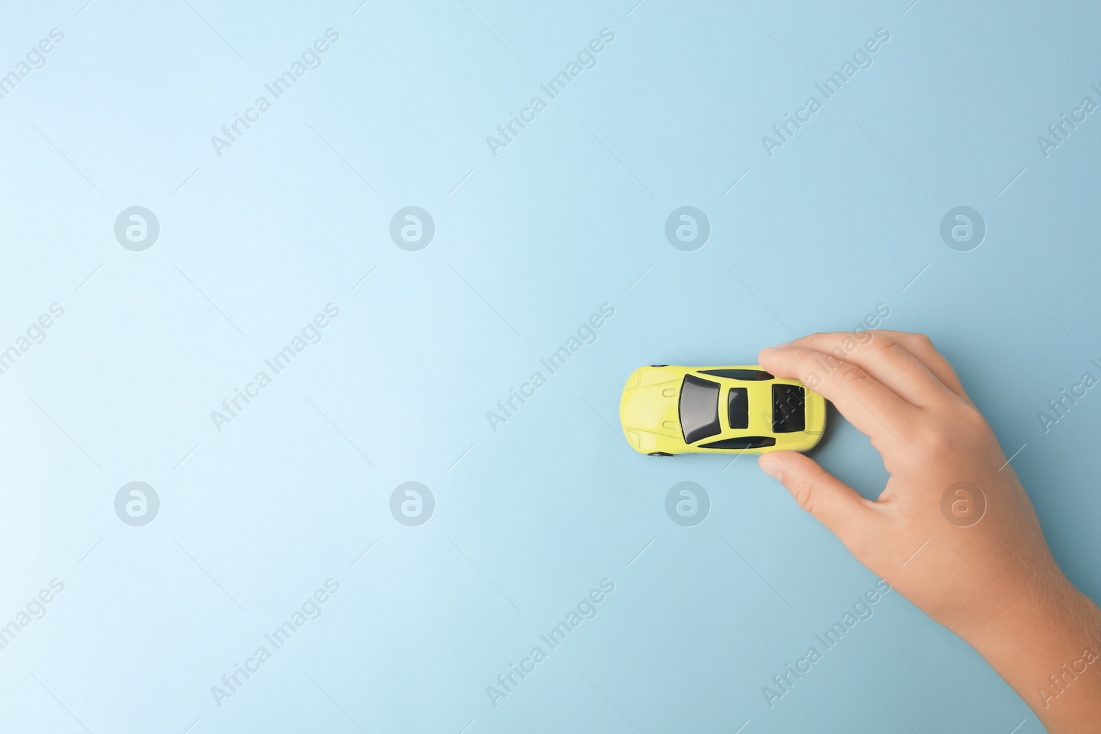 Photo of Child playing with toy car on light blue background, top view. Space for text