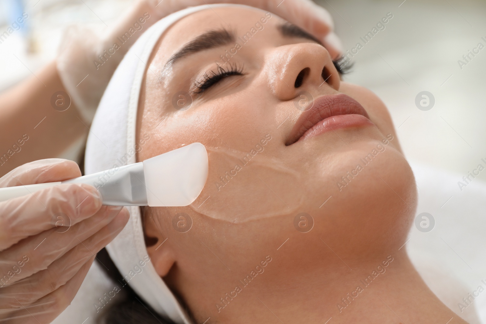 Photo of Young woman during face peeling procedure in salon, closeup