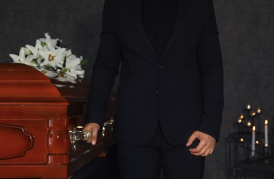 Young man carrying wooden casket in funeral home, closeup