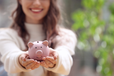Photo of Woman holding piggy bank against blurred background, closeup. Space for text