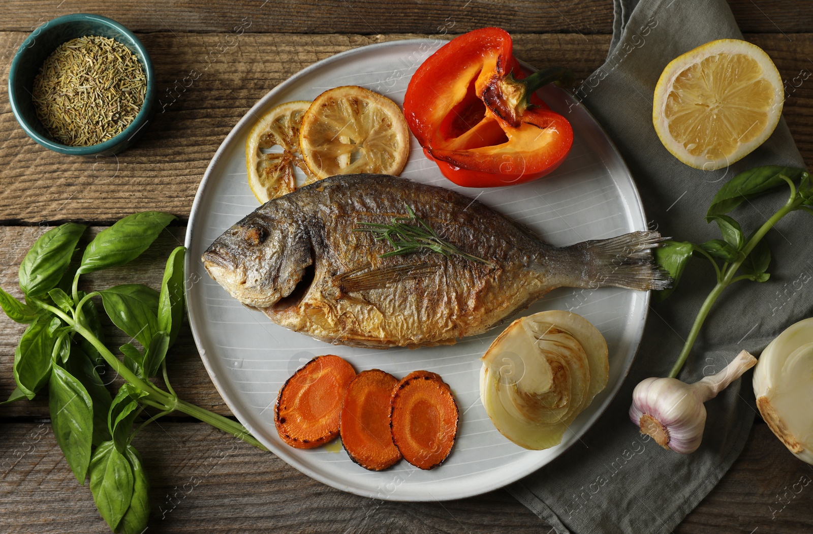 Photo of Delicious dorado fish with vegetables and herbs served on wooden table, flat lay