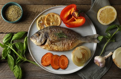 Delicious dorado fish with vegetables and herbs served on wooden table, flat lay