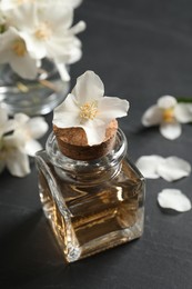 Photo of Jasmine essential oil and fresh flowers on dark grey table