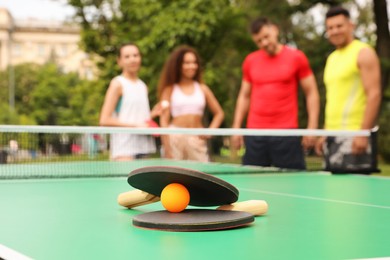 Photo of Friends talking near ping pong table outdoors, focus on rackets and ball