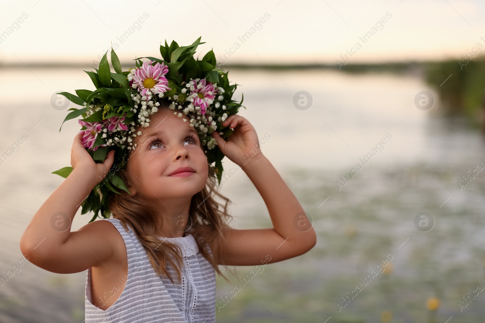 Photo of Cute little girl wearing wreath made of beautiful flowers near river