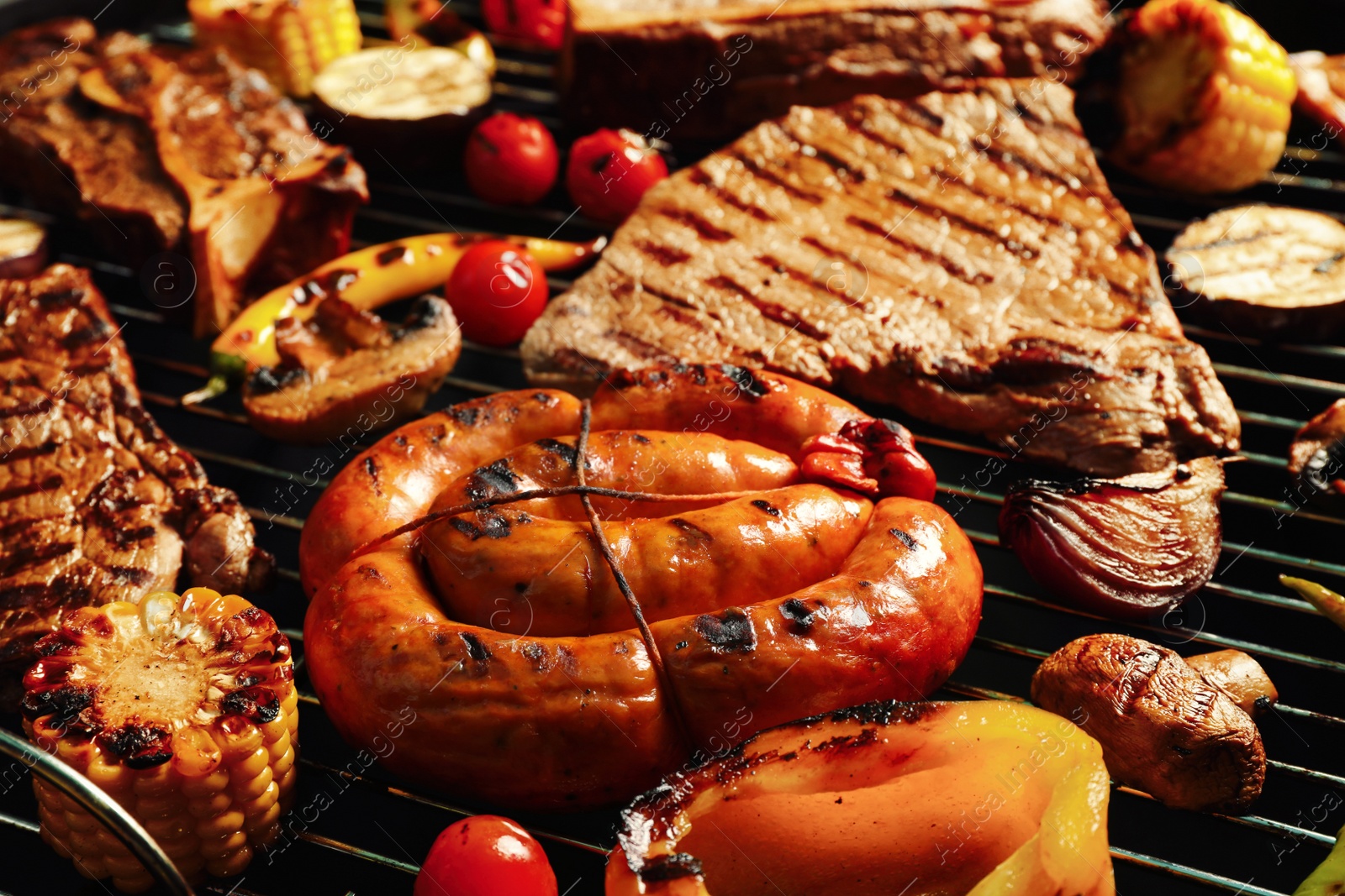 Photo of Fresh grilled meat steaks, sausage and vegetables on barbecue grate, closeup