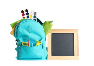 Photo of Backpack full of different school stationery and small blank chalkboard on white background. Space for text