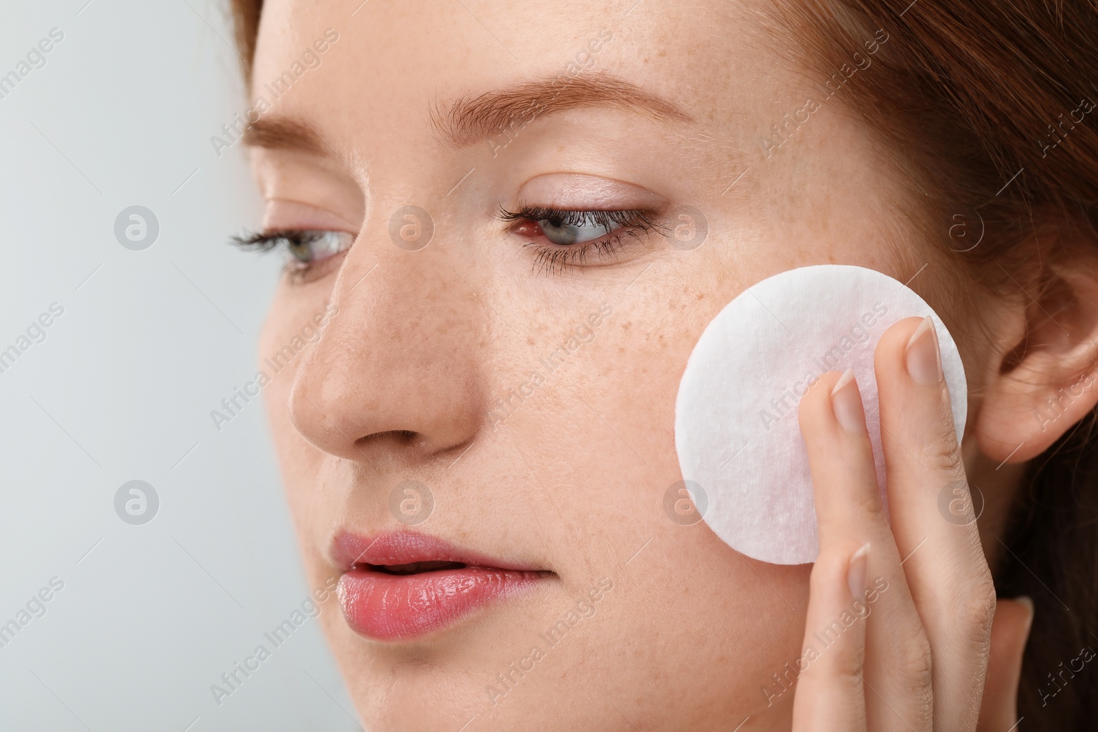 Photo of Beautiful woman with freckles wiping face on grey background, closeup