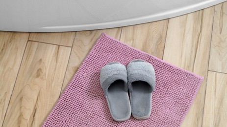 Photo of Mat with soft slippers near tub on wooden floor in bathroom, above view