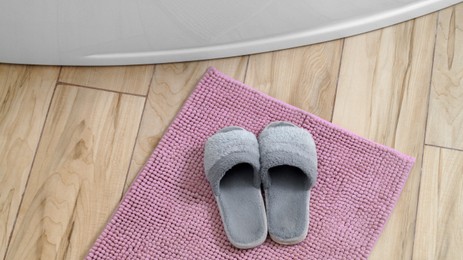 Mat with soft slippers near tub on wooden floor in bathroom, above view