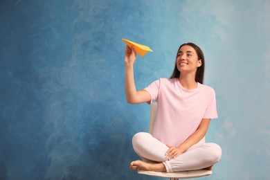 Beautiful young woman playing with paper plane on light blue background. Space for text
