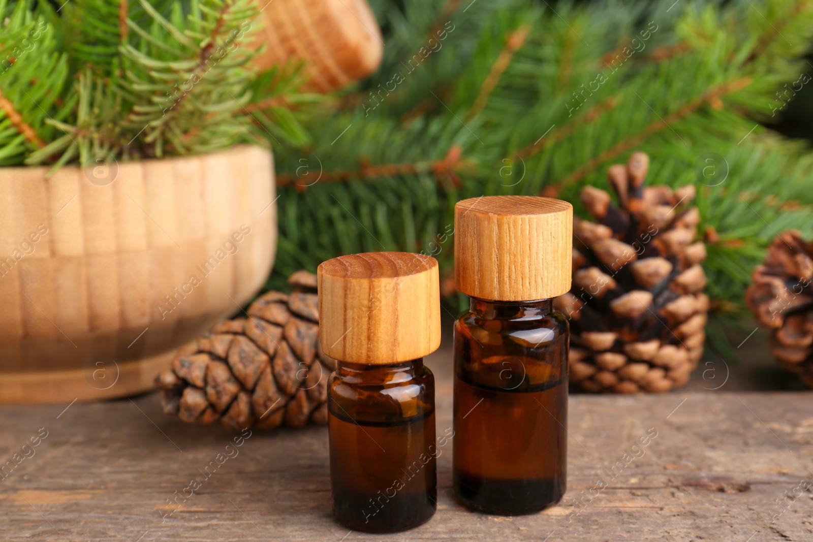 Photo of Bottles of pine essential oil, conifer tree branches and cones on wooden table, closeup