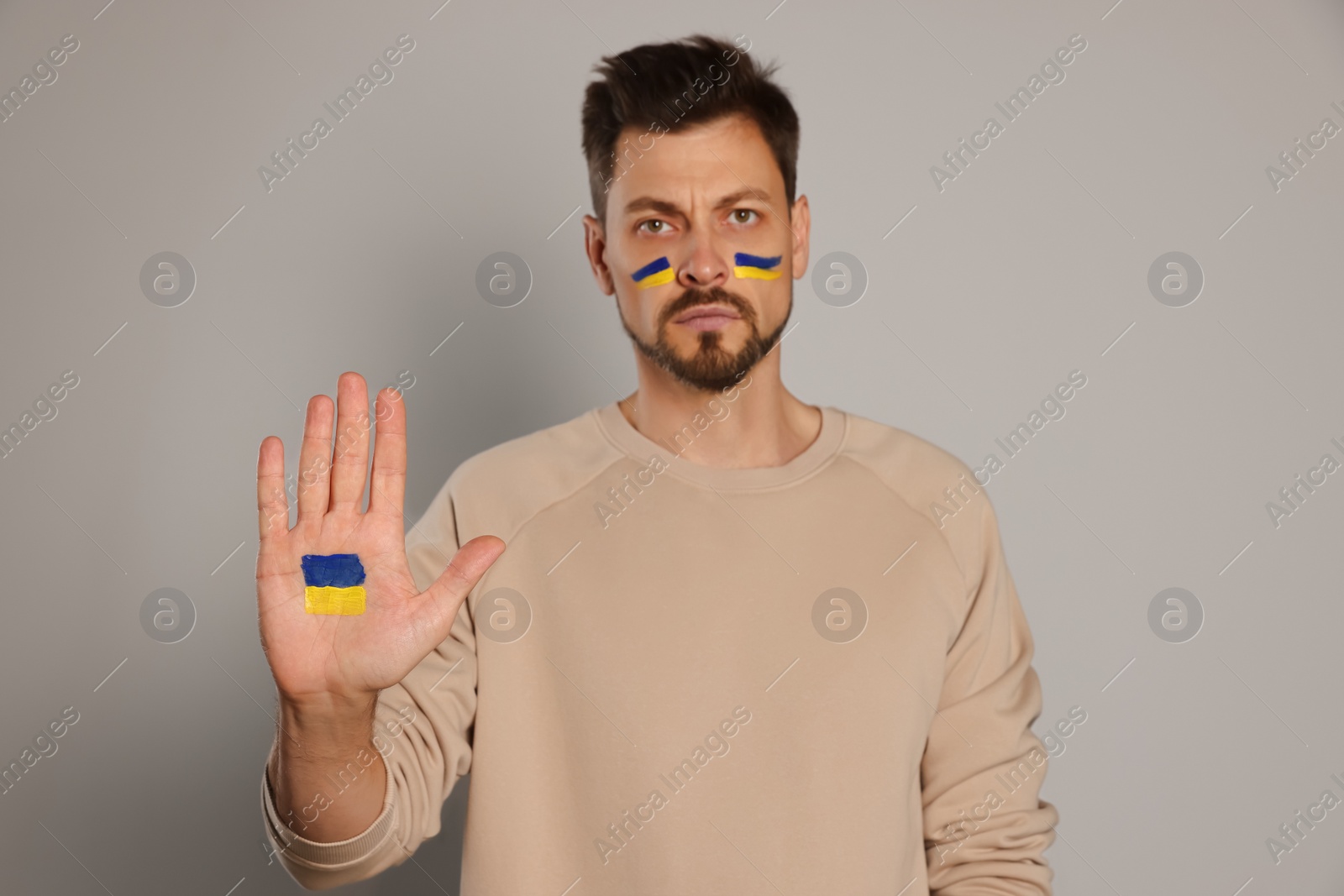 Photo of Angry man with drawings of Ukrainian flag against light grey background, focus on palm
