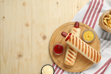 Delicious french hot dogs, fries and dip sauces on wooden table, flat lay. Space for text