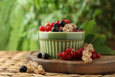Photo of Different fresh ripe currants and green leaf on wicker surface outdoors, closeup