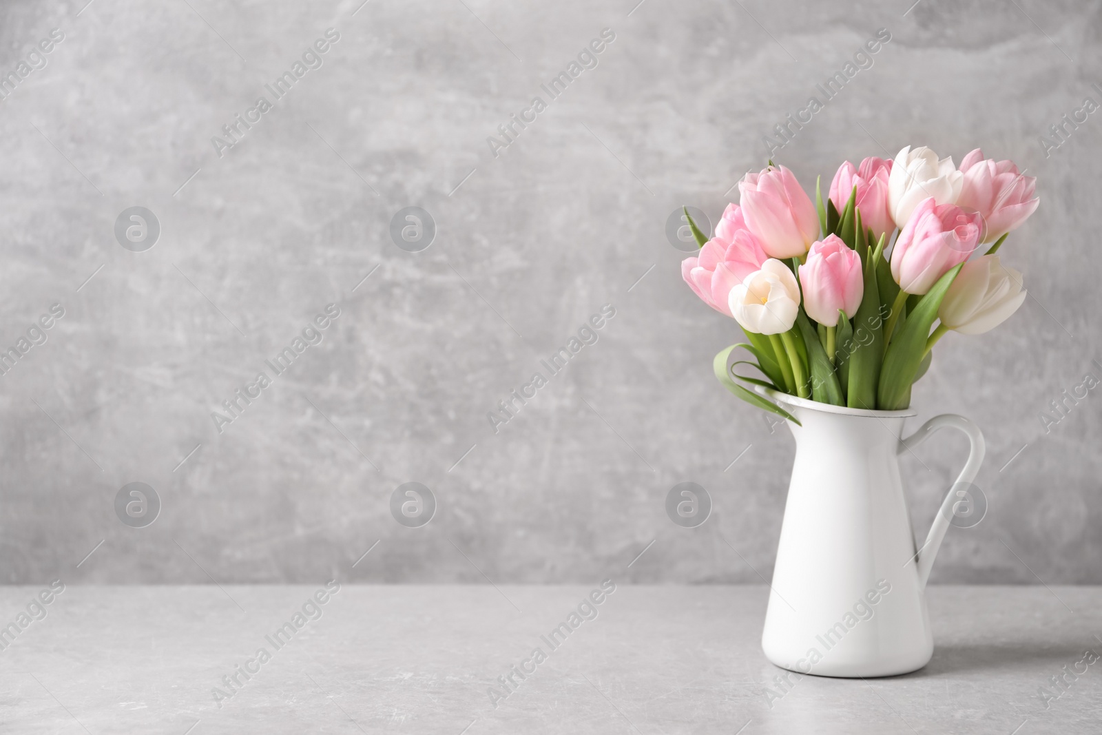 Photo of Beautiful bouquet of tulips in jug on light table. Space for text