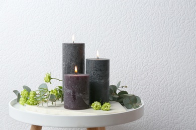 Set of burning candles, flowers and green branches on table at white wall, space for text