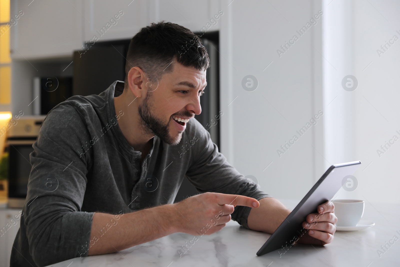 Photo of Emotional man with tablet at table in kitchen. Online hate concept