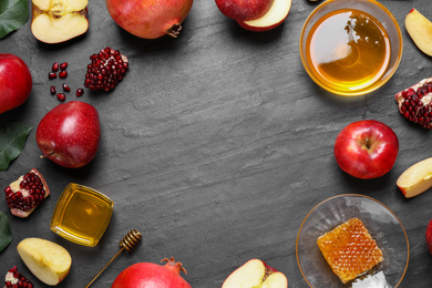 Photo of Frame of honey, apples and pomegranates on black table, flat lay with space for text. Rosh Hashanah holiday