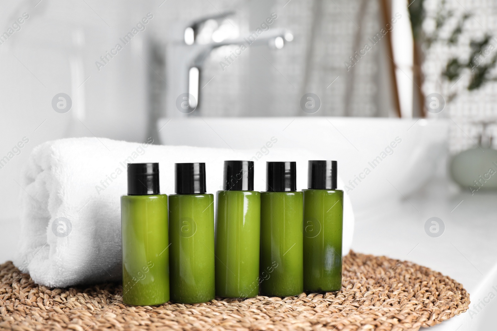 Photo of Mini bottles with cosmetic products and towel on wicker mat in bathroom