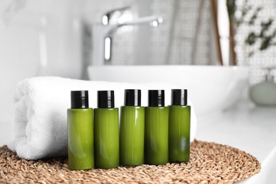 Mini bottles with cosmetic products and towel on wicker mat in bathroom