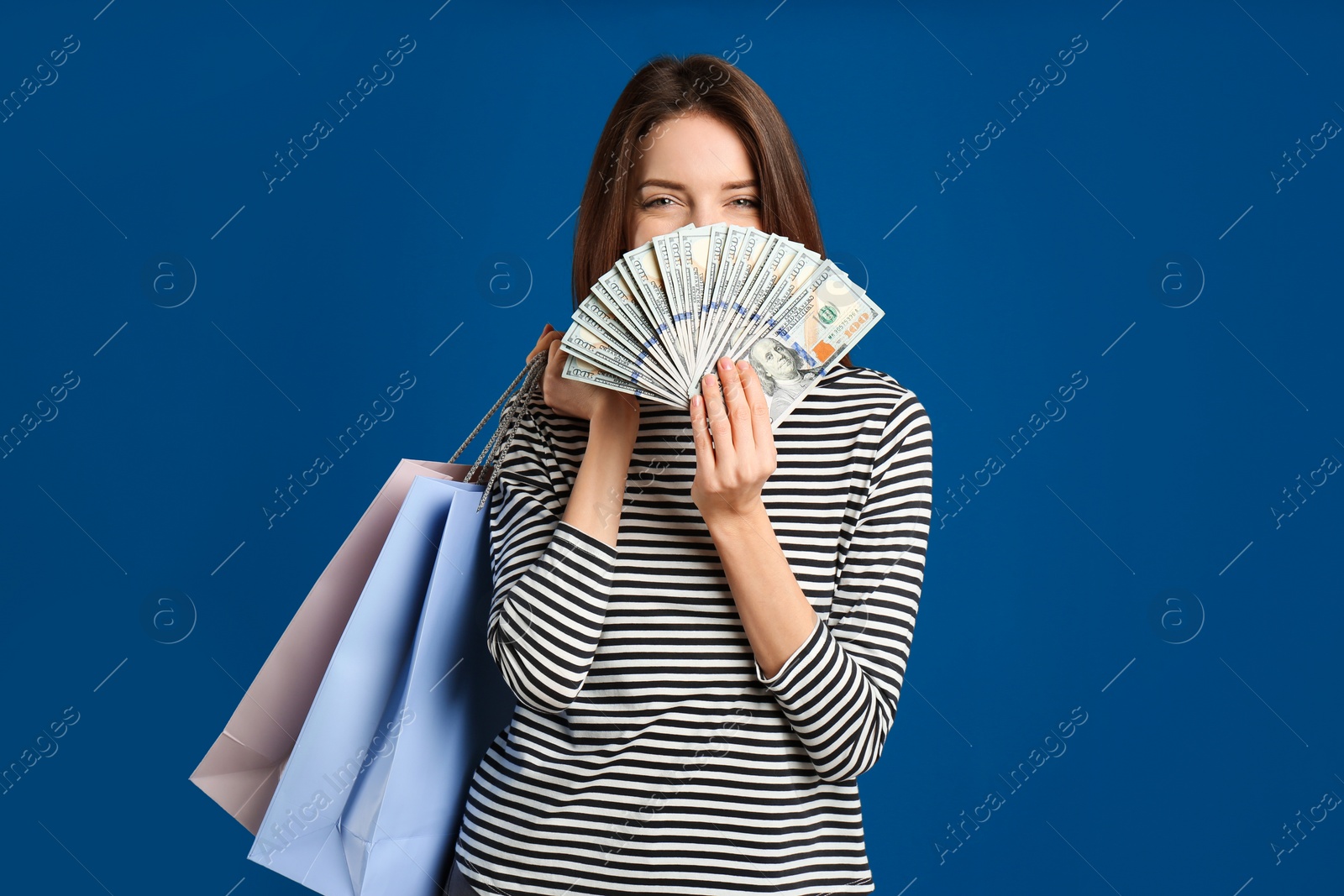 Photo of Young woman with cash money and shopping bags on blue background