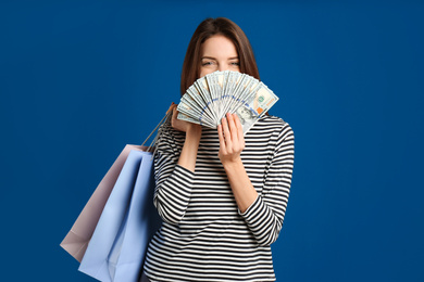 Young woman with cash money and shopping bags on blue background